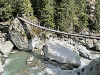 A hanging pedestrian bridge crosses the icy glacial river